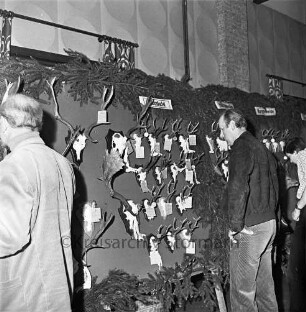 Kreisjägerschaft Stormarn e.V.: Rohlfshagen/Kupfermühle: Gastwirtschaft "Kupfermühle": Saal: Mitgliederversammlung: Ausstellungstafel mit Auswahl an Jagdtrophäen aus den Hegeringen: davor Personen bei der Besichtigung