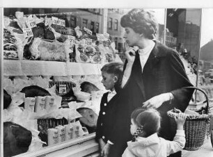 Eine Frau kauft mit ihren Kindern ein. Kritisch prüft sie die Preise in den Auslagen