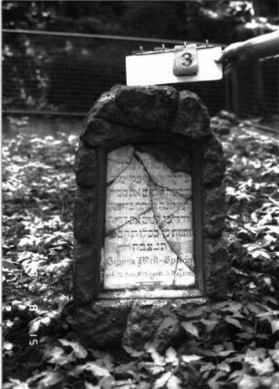 Grabstein 3 (Index: 100105641) Material: Muschelkalk, weiße Marmorplatte Zustand: Platte mehrfach gesprungen und teilweise herausgebrochen mit Textverlust Maße HxBxT: 106x53x32 cm Beschreibung: Stele, rustica, Rundbogenabschluß, Schriftplatte mit Segmentbogenabschluß: Grabstein 3