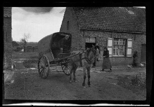 Nicht identifizierbare Ortschaft in Nordfrankreich oder Belgien: Einspänner mit Pferdekarren im Hof eines landwirtschaftlichen Anwesens, dabei eine Frau und ein junger Mann