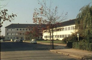 Kreisberufsschule [Ahrensburg]: Hermann-Löns-Straße: Gesamtansicht: rechts Altbau, links Erweiterungsbau: davor Straße, parkende Autos