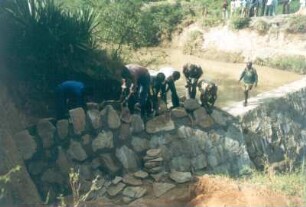 Kenia. Lumbwa-Erddamm Baustelle. Arbeiter beim Errichten einer Grundwassersperre aus Beton und Natursteinen in einem Fluß
