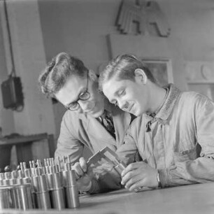 Lehrling bei Borgward misst ein Bauelement, der Ausbilder schaut zu