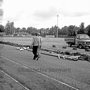 Sporteinrichtungen: Sportanlage am Kortenkamp: Grunderneuerung: Verlegung einer Entwässerungsleitung am Rand des Hauptspielfeldes: in der Mitte zwei Arbeiter: dahinter Rohre: rechts Lkw: hinten links Sportlerheim: hinten rechts Wohnhäuser: dahinter Bäume