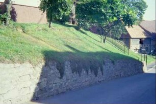 Natursteinmauer als Böschungsmauer, darüber Haus; Straße und Gebäude