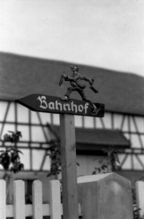 Alsfeld-Eifa (Vogelsbergkreis). Wegweiser mit geschnitzter Figur eines Reisenden
