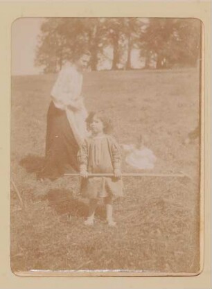 Eine Frau, ein Mädchen mit Rechen (Christiane) und ein Baby (Franz) auf einer Wiese in Aussee