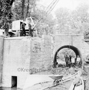 Brücke des Mühlenredder über dem Abfluss des Schlossgrabens: Renovierung: Seitenansicht von Süden: kein Durchfluss, Pumpe: Kran mit Greifarm, Arbeiter, Schubkarre, Baumaterial