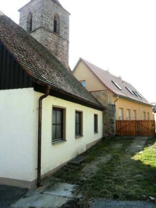 Ansicht von Nordosten mit Kirchturm (im Kern Gotisch) über neuzeitlichen Häusern sowie erhaltenem Teil der Kirchhofmauer (ohne Wehrgang)