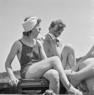Elisabeth Gremmler (links) und ein befreundeter Mann sitzen auf einem Segelboot, er spielt Mundharmonika