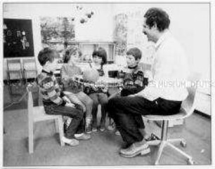 Sprecherzieher mit Kindern an einem Tisch (Altersgruppe 14-17)