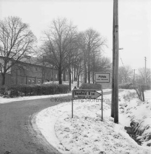 Dorfstraße: Landstraße Richtung Rehhorst und Reinfeld: vorn Ortseingang mit Ortsschild: hinten links Bauernhäuser hinter Bäumen: Winter