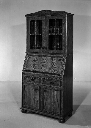 Schreibschrank mit Aufsatz : Ribnitz-Damgarten. VEB Möbelkombinat Ribnitz-Damgarten. Hausmesse, 1986. Schreibschrank mit Aufsatz. Holz, folienbeschichtet in Eichenholzoptik, rustikal (1986; VEB Möbelkombinat Ribnitz-Damgarten)