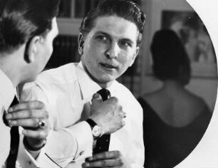 Ein junger Mann steht vor dem Spiegel und rückt die Krawatte gerade. Wer ist wohl der Schönste ? Aufgenommen 1963
