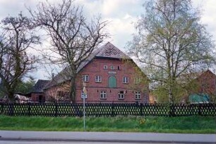 Bundesstraße (20): giebelständiges Bauernhaus aus Backstein: Straßenfront mit Sprossenfenstern, in Obergeschoss Ladeluke: Traufseite, hinten links Querbau mit Tor: rechts Nebengebäude mit Verbretterung: vorne Bäume, Jägerzaun