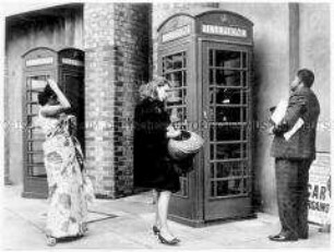 Drei wartende Menschen vor einer britischen Telefonzelle