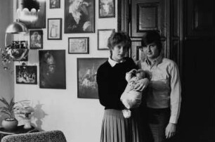 Familie W. im Wohnzimmer, an der Wand sind zahlreiche Reproduktionen bekannter Gemälde zu sehen (u. a. Raffaels "Sixtinische Madonna", Liotards "Schokoladenmädchen", Rembrandts "Mann mit dem Goldhelm", Rembrandts "Selbstbildnis mit seiner Frau Saskia")