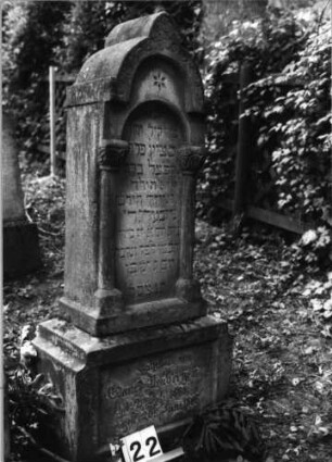 Grabstein 122 (Index: 100079731) Material: Sandstein Zustand: verwittert mit Textverlust Maße HxBxT: 130x36x23 cm Beschreibung: ädikularartige Stele mit Halbsäulen, Sockel, eingezogener Rundbogenabschluß mit Mittelakroter, Schriftfeld eingetieft Symbolik: Sternchen, Ranken Besonderheit: Kindergrab: Grabstein 122