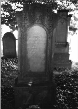 Grabstein 334 (Index: 100085183) Maße HxBxT: 187x73x30 cm Beschreibung: Stele, profilierter Sockel, giebelart. Abschl. , rechteck. erhöht, Schrift eingetieft Symbolik: Mohnkapseln: Grabstein 334