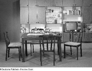 Eßtisch (Modell T 321/5) mit vier Stühlen (Stuhl mit gepolsterter Sitzfläche (Modell N 30)) (1980; VEB Vereinigte Sitzmöbelindustrie Neuhausen). Ansicht mit Anbauwand