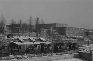 Blick auf eine Industrieanlage im Winter, im Vordergrund ein Wasserlauf mit Befestigung und Werksbahnanlagen