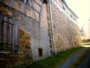 Nordflanke mit Kirchhofmauer und Gaden von Nordosten (Kirchhofmauer als Außenmauer der Gaden mit Wehrgang und Schießscharten im oberen Bereich unterhalb der Fachwerk-Gadengeschosse)