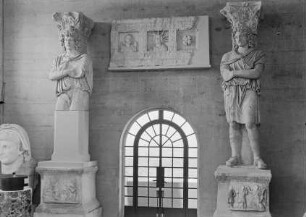 Zwei Statuen auf reliefierten Sockeln: Barbar mit phrygischer Mütze. In der Mitte Fragment einer Kassettendecke mit Reliefdarstellungen