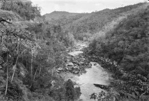 Flusslandschaft : Ein Flusslauf zwischen Hügeln hindrch. Im Flussbett befinden sich zahlreiche Felsen. An den Hängen Wald, auf dem linken eine Straße.
