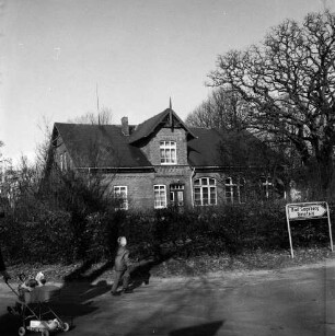 Steinfeld: Kreisstraße Richtung Reinfeld: vorn rechts Straßenschild: dahinter Wohnhaus [ehemalige Volksschule] mit Garten und Hecke: hinten rechts Baum: vorn links Kinderwagen und Kind