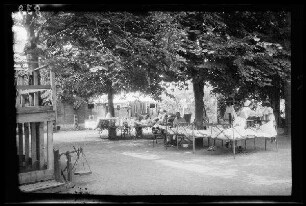 Origny (=Origny-Sainte-Benoite, Dep. Aisne, Frankreich): Krankenschwester und Patienten auf einfachen Feldbetten im "Hof eines Lazaretts" unter Laubbäumen (Distanzaufnahme)
