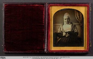Alte Frau mit Haube und Brille in der Hand haltend