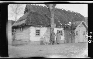 2 Offiziere und eine Einheimische vor einem landestypischen Holzhaus