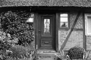 Schulstraße 27: traufständige Fachwerkkate mit Reetdach: Straßenfront, Detailaufnahme: Eingangstür, beiderseits Sprossenfenster, Hausnummer: 21. September 1994