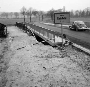 Trave: Brückenneubau: Spannbetonbrücke nach Fertigstellung: links alte Holzbrücke: im Vordergrund Straßenschild Richtung Reinfeld und VW-Käfer: hinten Wiesen und Baumreihen