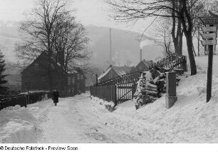 Blick von einer verschneiten Straße auf ein bewohntes Tal