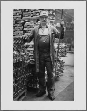 Mann mit Arbeitskittel und Schutzhelm vor Metallteilen