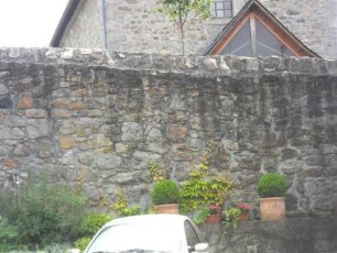 Treis an der Lumda-Evangelische Kirche - Kirchhofmauer (Wehrgang mit Steinbrüstung und Schießscharten abgetragen) im Westen mit Werksteinen im Mauersteinverband über Ortsseite