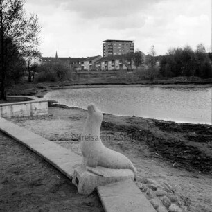 Realschule Harksheide: Fadens Tannen: Kunst im öffentlichen Raum: Steinskulptur einer Robbe mit Steinhaufen auf kleiner Mauer: dahinter Teich auf dem Schulgelände: dahinter Wohngebäude an der Rathaustwiete: im Hintergrund das Rathausgebäude: hinten rechts und links Bäume