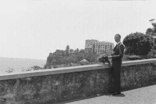 Reisefotos Madeira. Der Bordfotograf Franz Grasser mit Blumenstrauß und Kamera an einer Mauer oberhalb eines Hafenbeckens