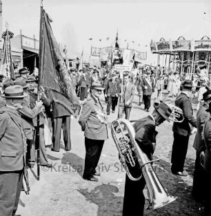 Schützenfest: Veranstalter Bürgerschützengilde von 1627 e.V. Bad Oldesloe: Umzug: Aufmarsch auf Festplatz an Sehmsdorfer Straße: Schützenkapelle, Schützenvereine mit Fahnen, darunter Schützenverein aus Lübeck sowie Schützengilde aus Kiel-Elmschenhagen: hinten Kinderkarussell, Jahrmarktstände, Festbesucher, 28. Juni 1959