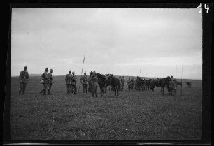 Soldaten mit Pickelhelmen neben aufgestellten Lanzen und einigen Pferden auf einem weiten Feld