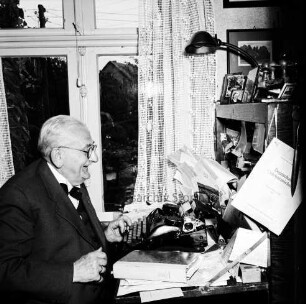 Clasen, Martin: geboren 1882, gestorben 9. November 1962: von 1909 bis 1924 evangelischer Pastor in Neustadt, von 1924 bis 1947 Pastor in Reinfeld; Heimatforscher, Begründer des Heimatmuseums Reinfeld, ehrenamtlicher Archivpfleger: Einwohner von Reinfeld: Aufnahme aus Anlass seines 50-jährigen Amtsjubiläums als Geistlicher, an seinem Arbeitsplatz vor Schreibmaschine: Träger des Bundesverdienstkreuzes am Bande