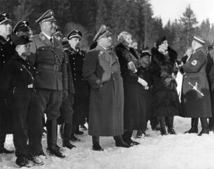Dr. Robert Ley, Reichsleiter der NSDAP und Leiter der Deutschen Arbeitsfront mit Anhang (links ein politischer Leiter der NSDAP, daneben ein Pimpf der Deutschen Jungend, hinter Ley ein SS-Angehöriger, ganz rechts ein SA-Führer) und Frauen bei einer winterlichen Sportvorführung