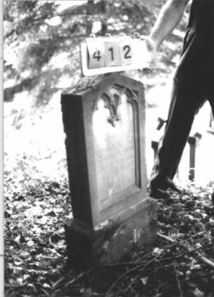 Grabstein 412 (Index: 99800302) Material: Sandstein Zustand: leicht verwittert Maße HxBxT: 88x35x13 cm Beschreibung: Stele, flacher Giebelabschluß, Schriftfeld eingetieft in Maßwerkform, Sockel Besonderheit: Kindergrab: Grabstein 412