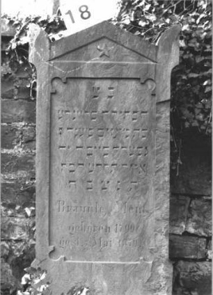 Grabstein 18 (Index: 100114426) Material: Sandstein Zustand: teilweise abgeblättert Maße HxBxT: 142x54x10 cm Beschreibung: Stele, Sockel, giebelartiger Abschluß mit Eckakroteren, Schriftfeld rechteckig Symbolik: fünfzackiger Stern: Grabstein 18