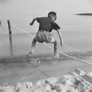 Kind der Gremmlers springt über ein aufgespanntes Seil am Strand von Henkenhagen (heute: Ustronie Morskie)