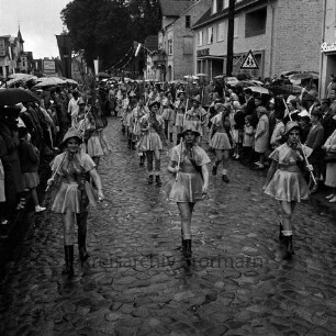 Karpfenfest: Umzug: Paul-von-Schoenaich-Straße: Fischerinnengarde mit Keschern: an den Straßenrändern Zuschauer, mit Regenschirmen: im Hintergrund Fahnenschmuck, Wimpelgirlanden, Bäume des Kirchhofs, 8. Oktober 1961