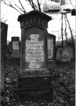 Grabstein 190 (Index: 99752053) Material: Sandstein Zustand: leicht verwittert Maße HxBxT: 148x38x27 cm Beschreibung: konische Stele, getreppt. Sockel, giebelart. Abschl. m. Verdach. , Schriftfeld eingetief Symbolik: gestelztes Rundbogenfries: Grabstein 190