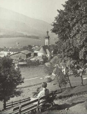 Reit im Winkl (Oberbayern). Blick auf die Stadt. In der Bildmitte die Pfarrkirche St. Pekratius. Eine Frau sitzt auf einer Bank