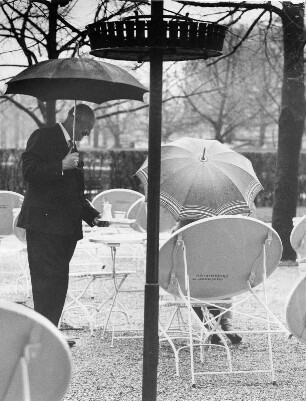 München. In einem Garten-Cafe im Englischen Garten wird auch bei Regenwetter serviert. Der Kellner trägt Schirm